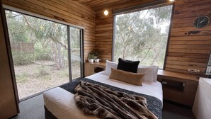 Camera da letto con un letto grande, pareti in legno e vista sugli alberi attraverso ampie finestre.