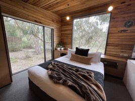 Un dormitorio con una cama grande, paredes de madera y vistas a árboles a través de amplias ventanas.