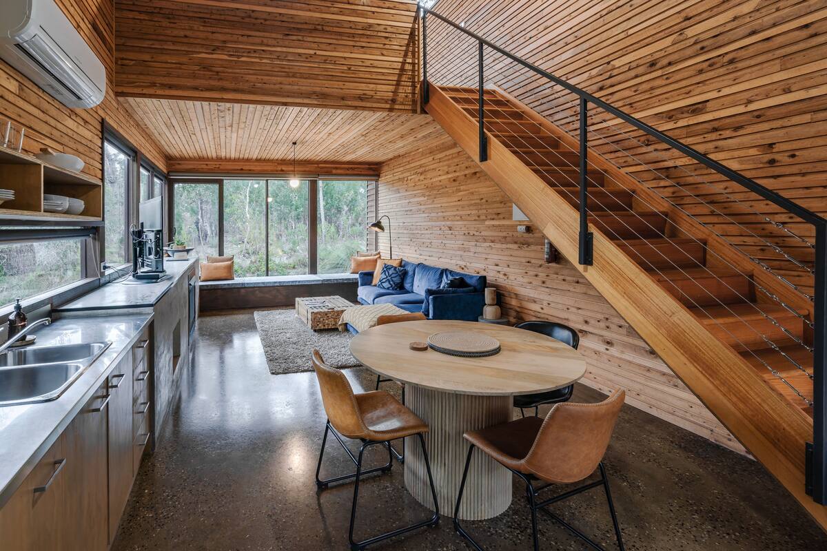 Una cocina moderna con una isla central, paredes de madera y una escalera.