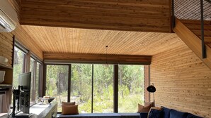 Un interno moderno con soffitto in legno, ampie finestre, angolo cottura e zona salotto con divano blu.