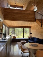 Un interior moderno con techo de madera, ventanas amplias, una zona de cocina y un área de descanso con un sofá azul.