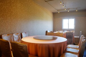 Zona pranzo con tavoli rotondi e sedute imbottite, parete decorata e finestra che lascia entrare luce naturale.