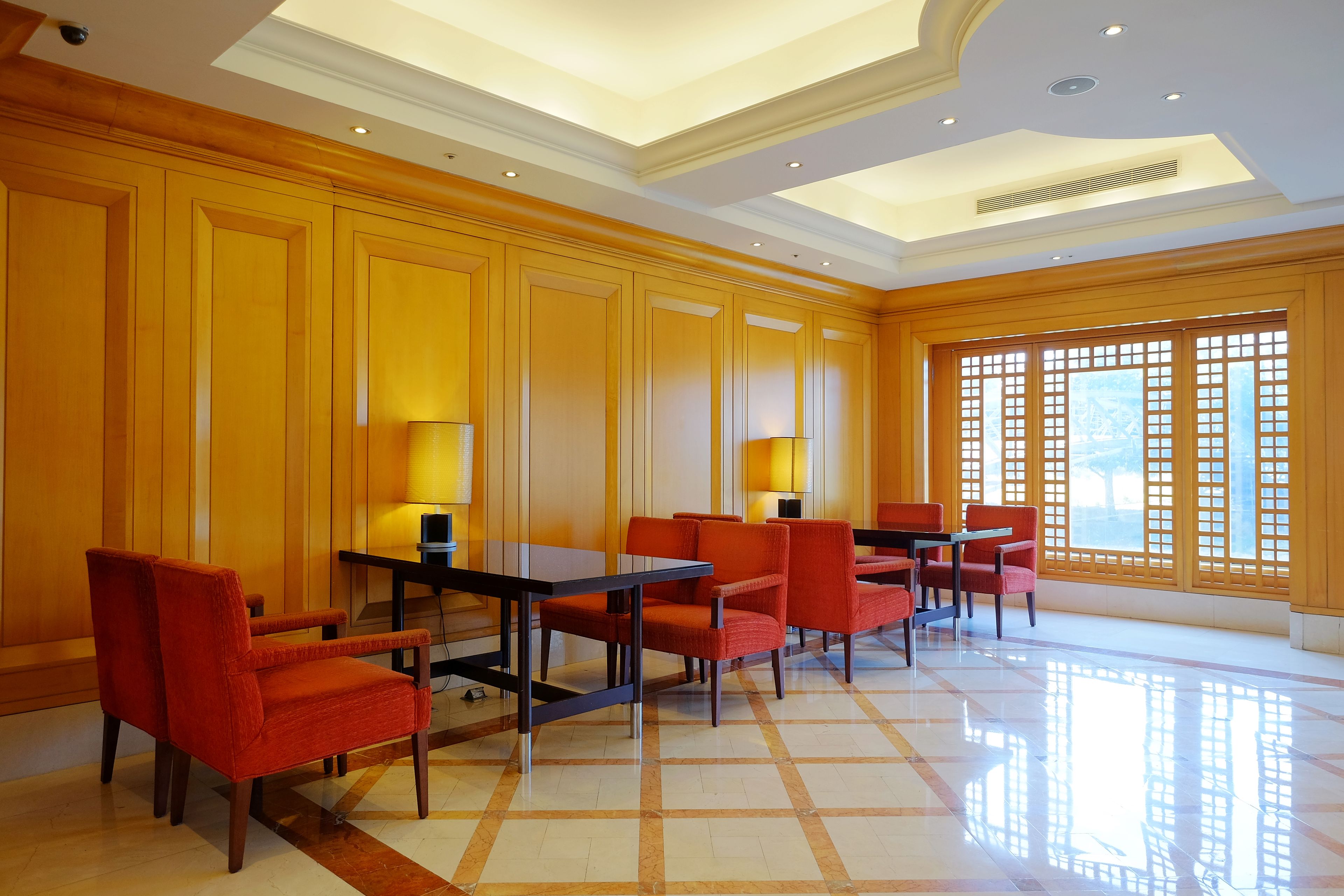 Un hall de hotel con paneles de madera, suelo de baldosas y un área de estar con mesas y sillas.