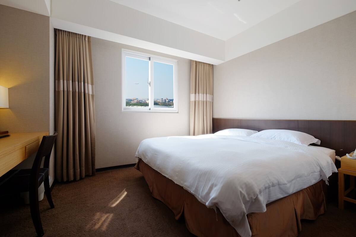 Een hotelkamer met een groot bed, een bureau en een raam met gordijnen.