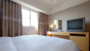 Une chambre d’hôtel avec un grand lit, un téléviseur à écran plat, un bureau avec une lampe et une fenêtre avec des rideaux.