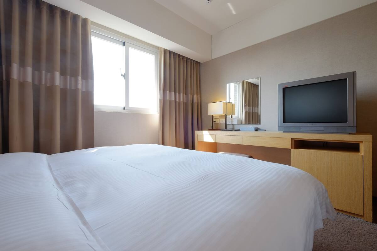 Hotelkamer met een groot bed, een flatscreen televisie, een bureau met lamp en een raam met gordijnen.