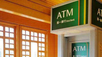 An ATM machine with a sign above it, a window with a wooden lattice design, and a wall with a textured pattern.
