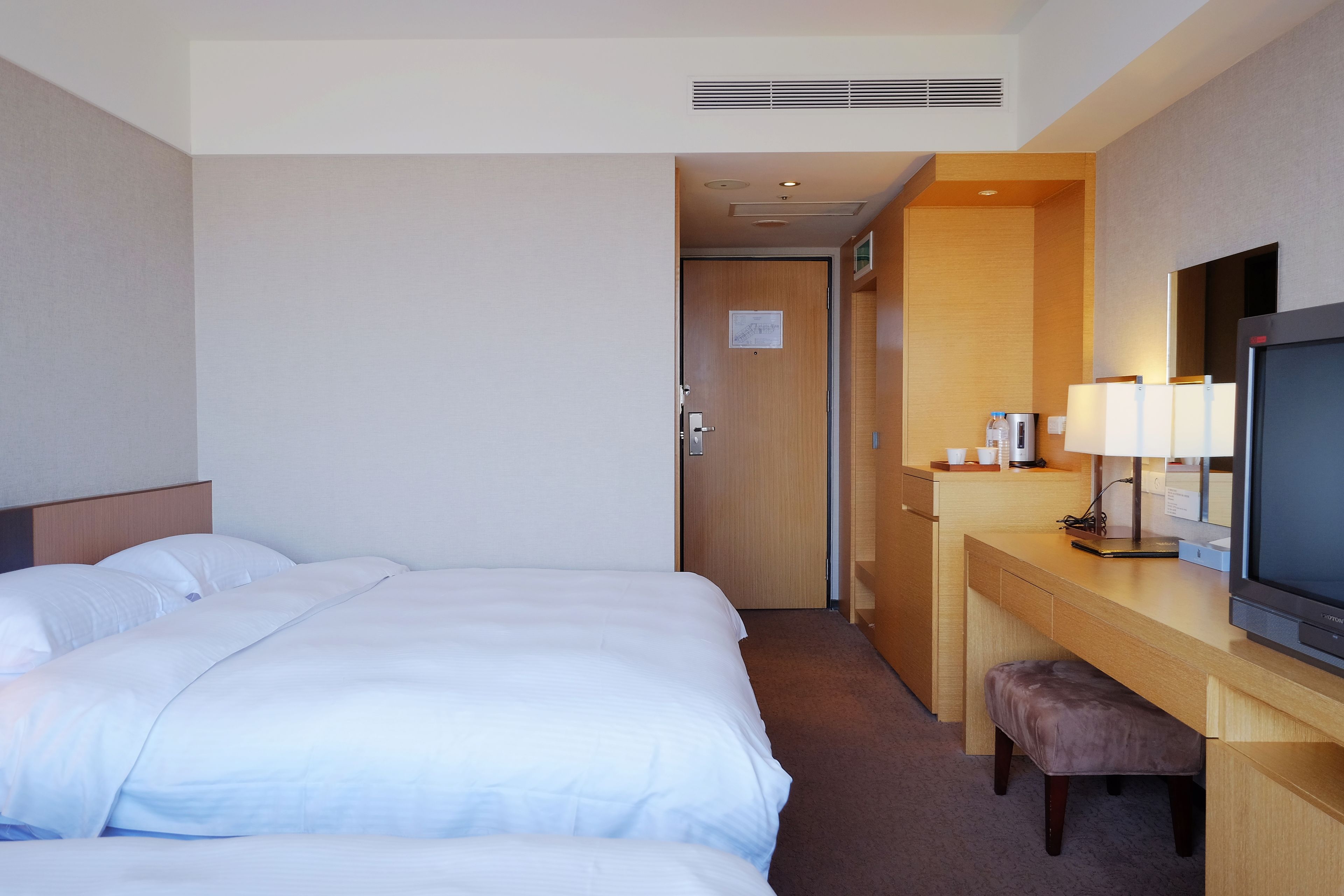 Una habitación de hotel con una cama grande, un escritorio con televisor y un pequeño banco.