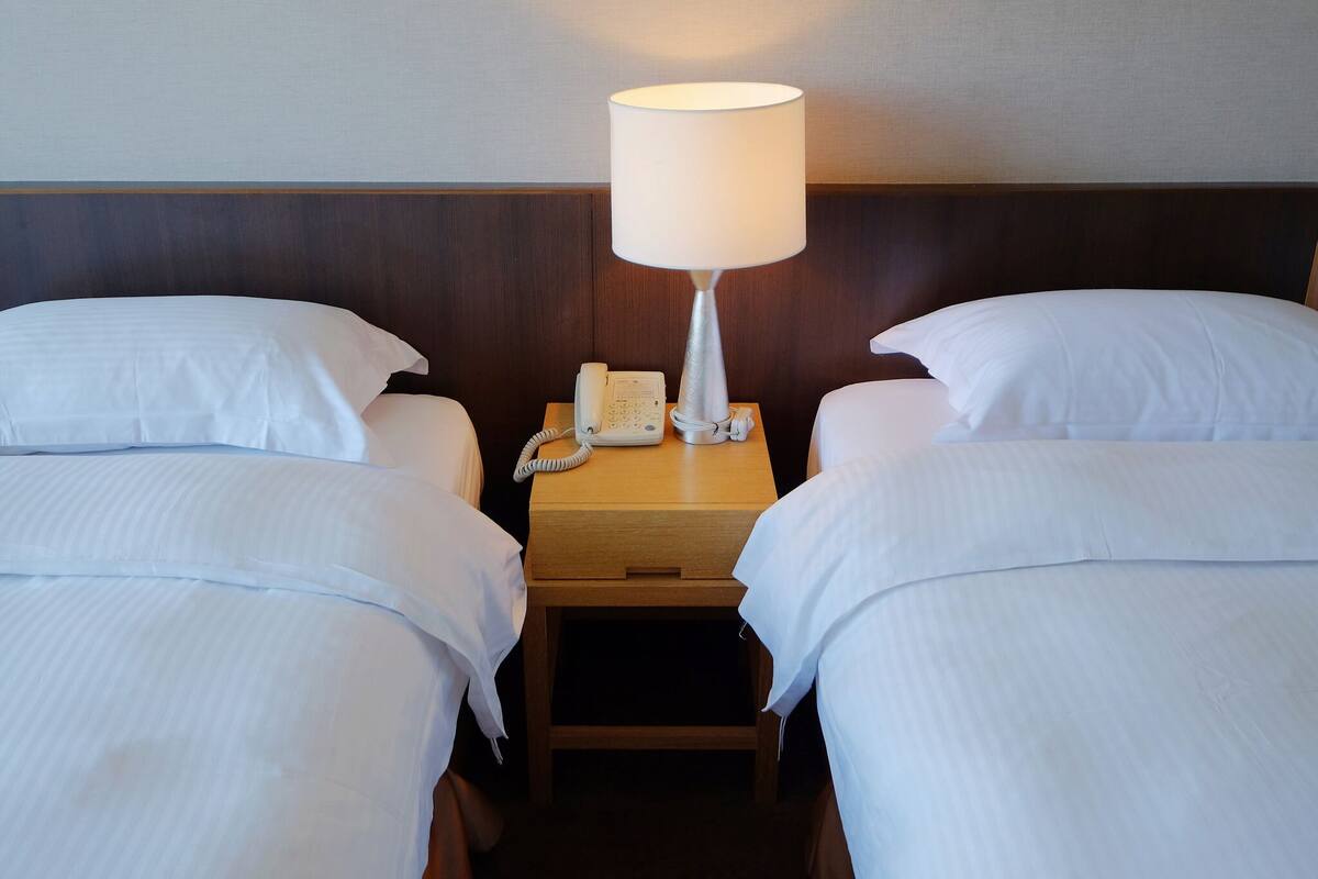 Een hotelkamer met twee bedden, elk voorzien van witte lakens, een nachtkastje met een lamp en een telefoon.