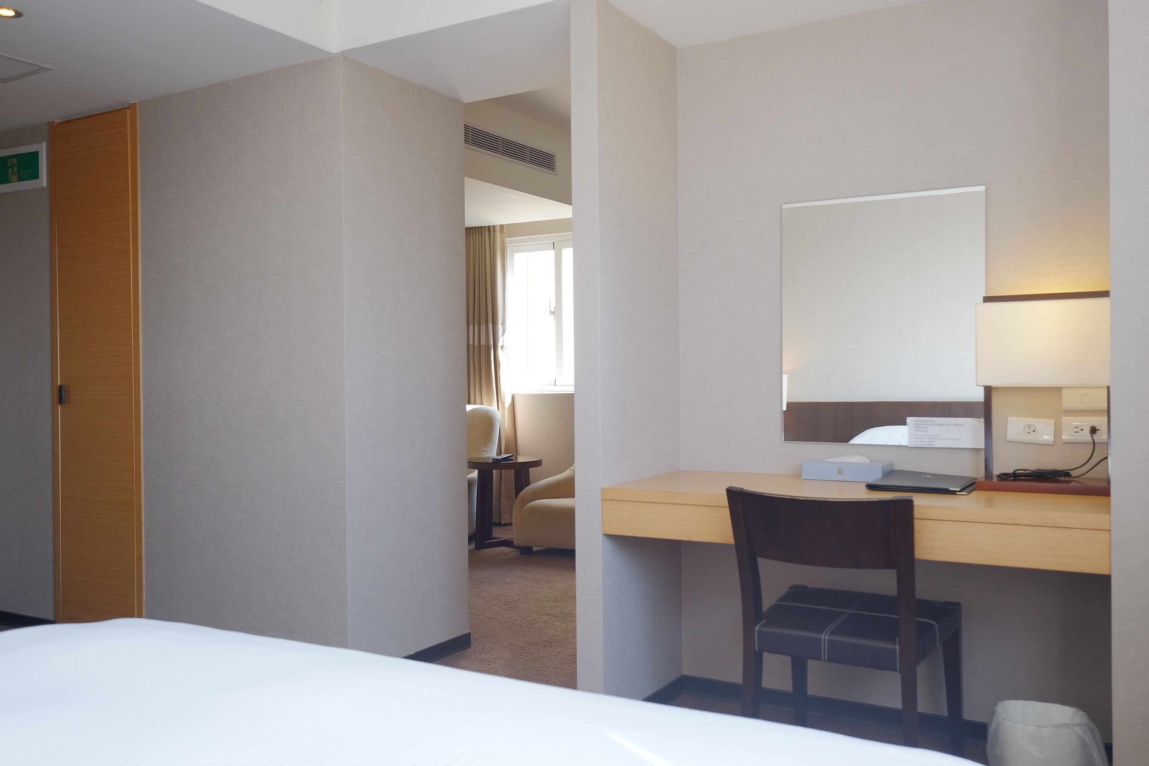 A hotel room with a bed, a desk with a chair, a small table, and a mirror.