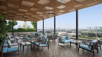A covered outdoor seating area with multiple chairs and tables, large windows offering a city view.