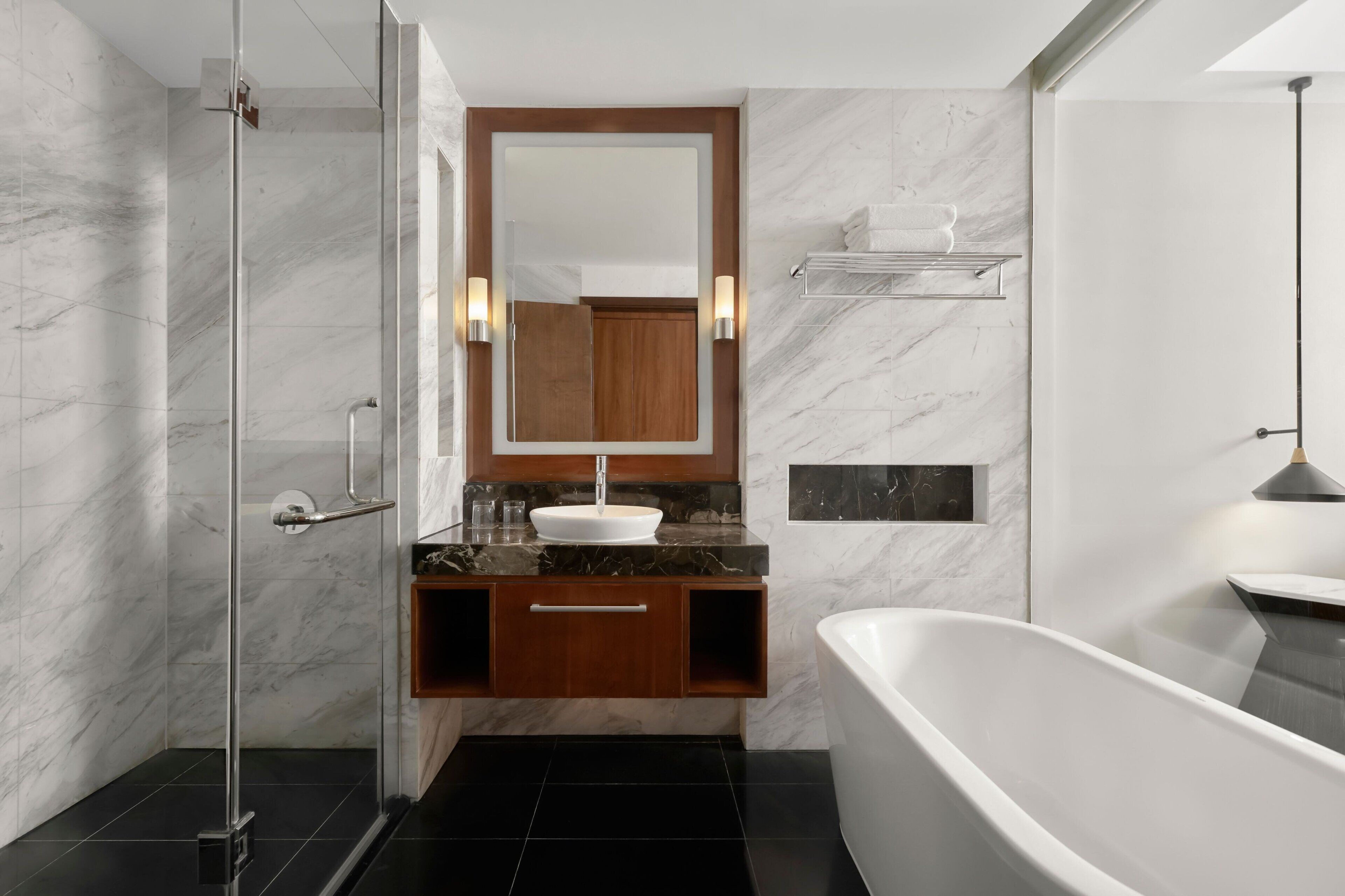 A modern bathroom with a glass-enclosed shower, a freestanding bathtub, and a wooden vanity with a marble countertop.