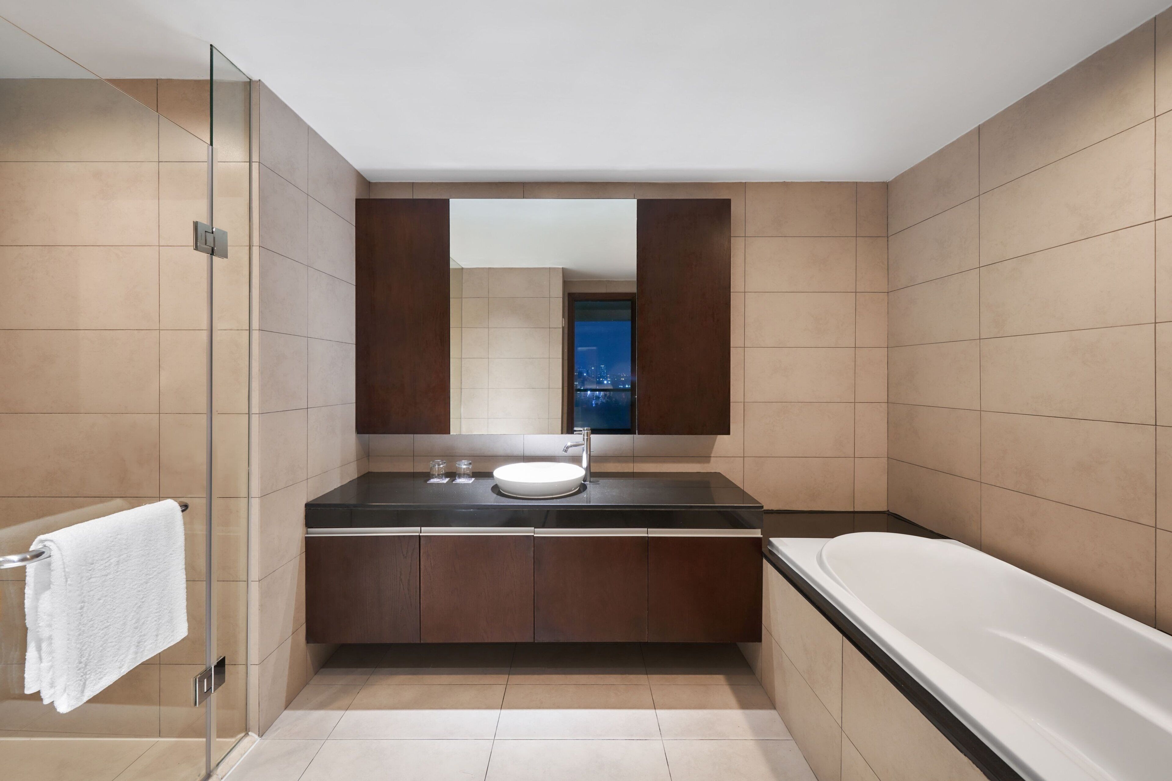 A modern bathroom with a glass shower enclosure, a large mirror, a built-in sink, and a bathtub.