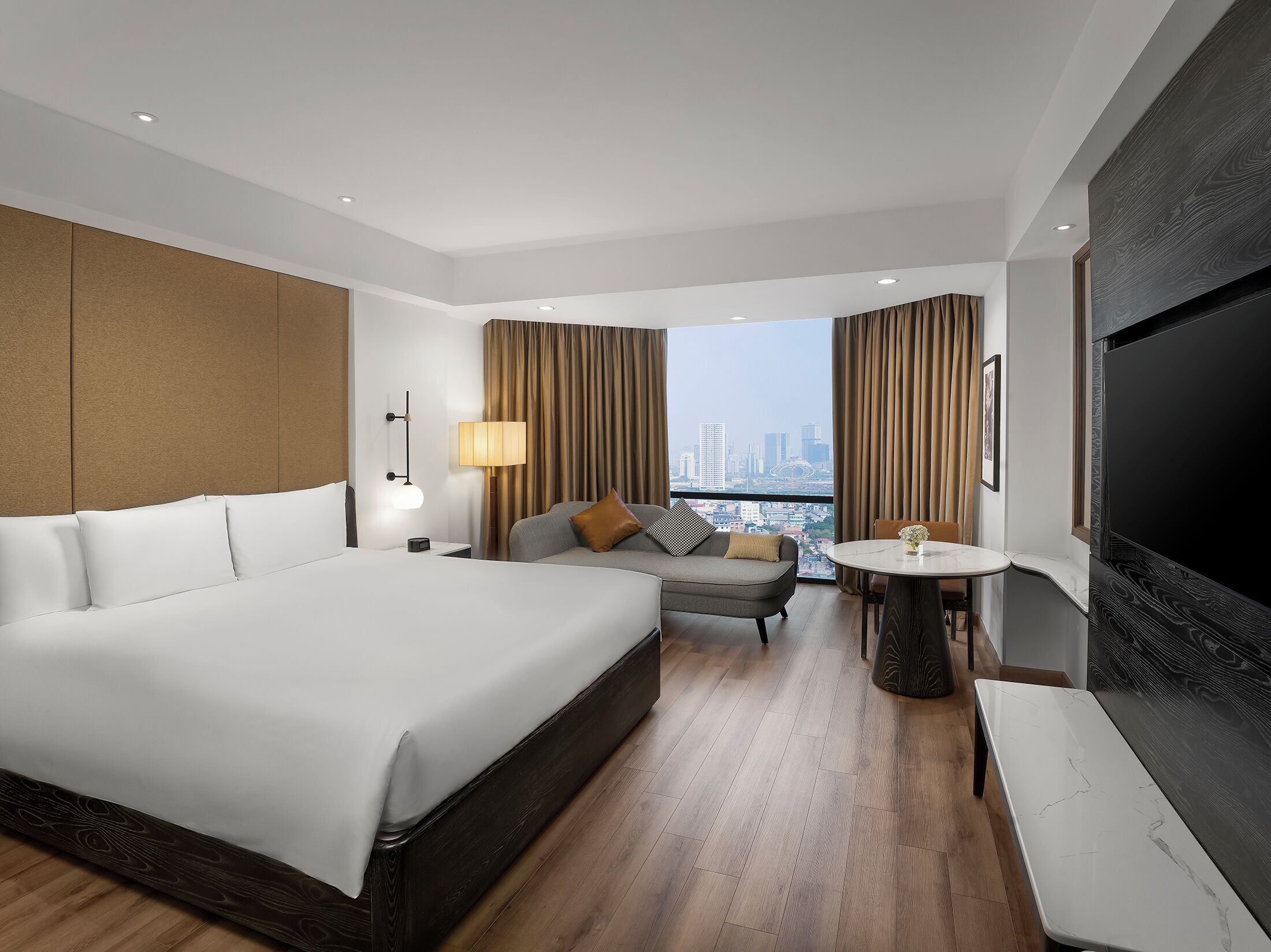 A modern hotel room with a large bed, a sofa, a small table, and a TV.