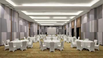Un amplio salón de conferencias con varias mesas redondas y sillas blancas, equipado con luces en el techo y una pantalla grande al frente.