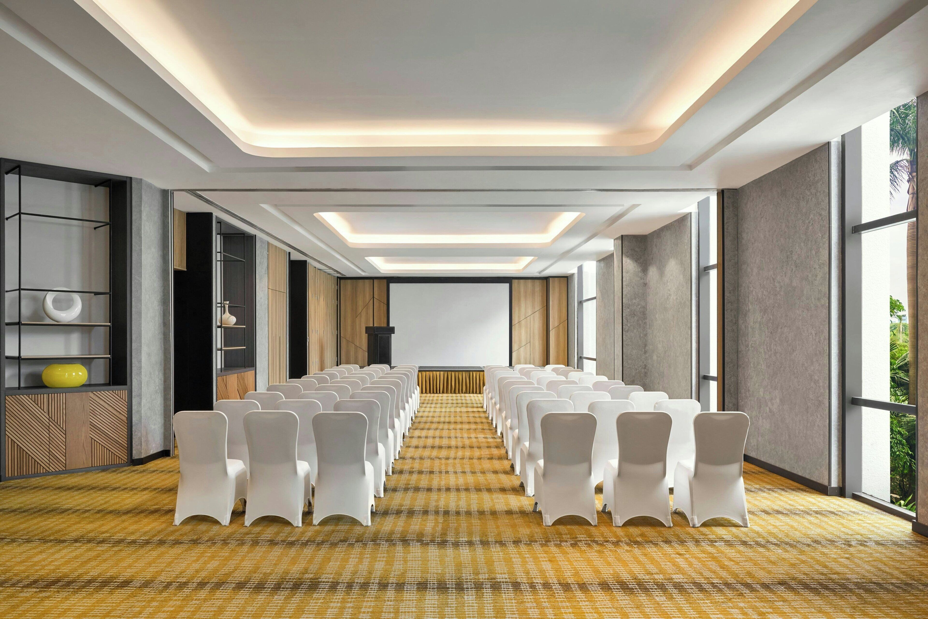 A conference room with rows of white chairs, a checkered carpet, and a modern ceiling design.