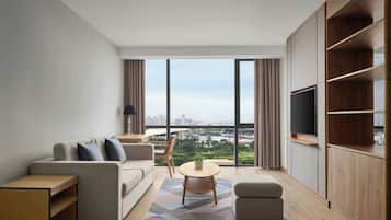 Una sala de estar moderna con un sofá, una mesita y un televisor. La habitación tiene ventanas amplias con vistas a un paisaje urbano.