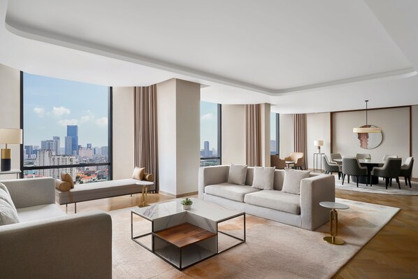 Ein modernes Hotelzimmer mit großem Fenster und Blick auf die Stadt, einer Sofagarnitur, einem Essbereich und einem schlichten Couchtisch.