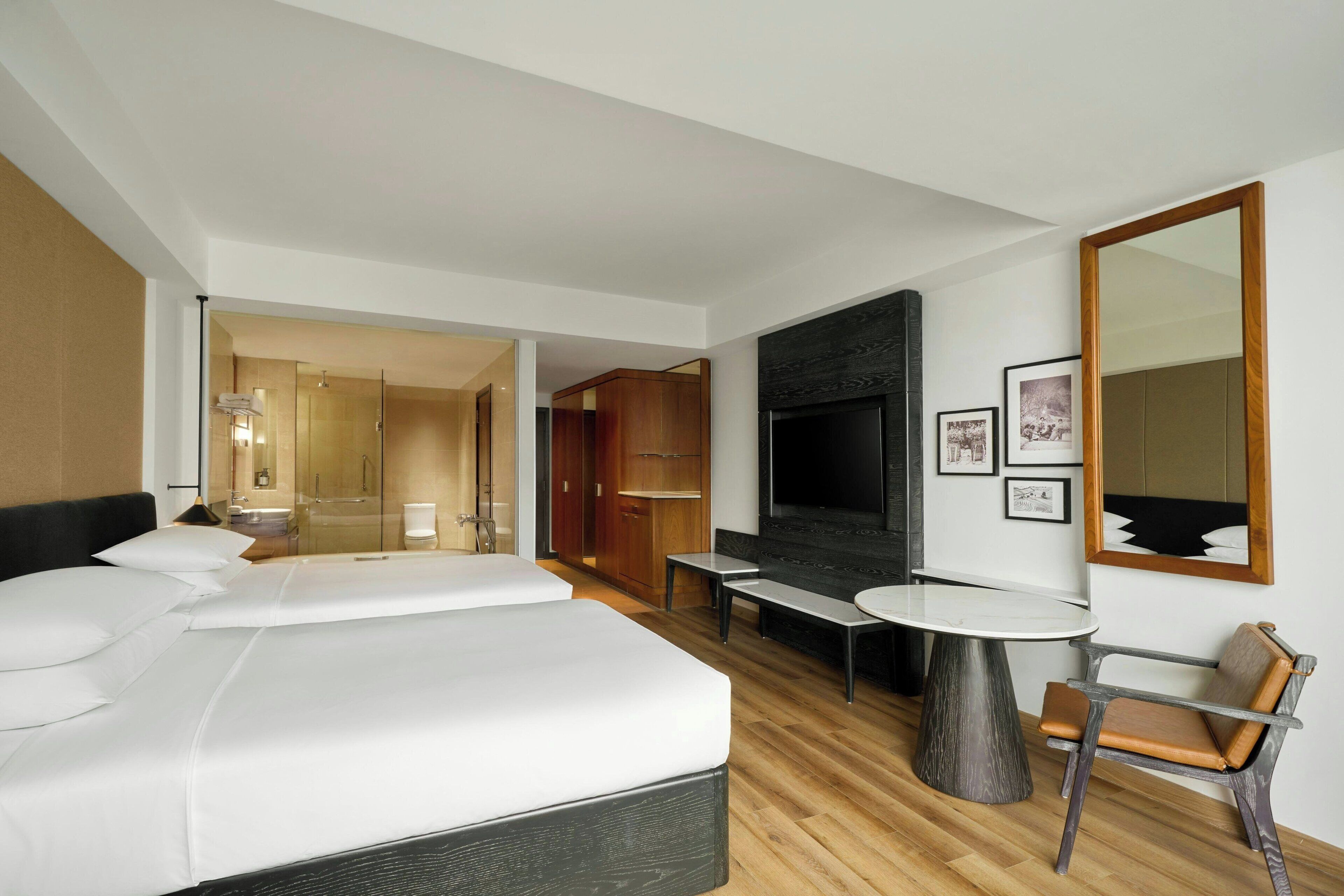 Una habitación de hotel con una cama grande, un televisor, una zona de estar con una mesa y sillas, y un espejo en la pared.
