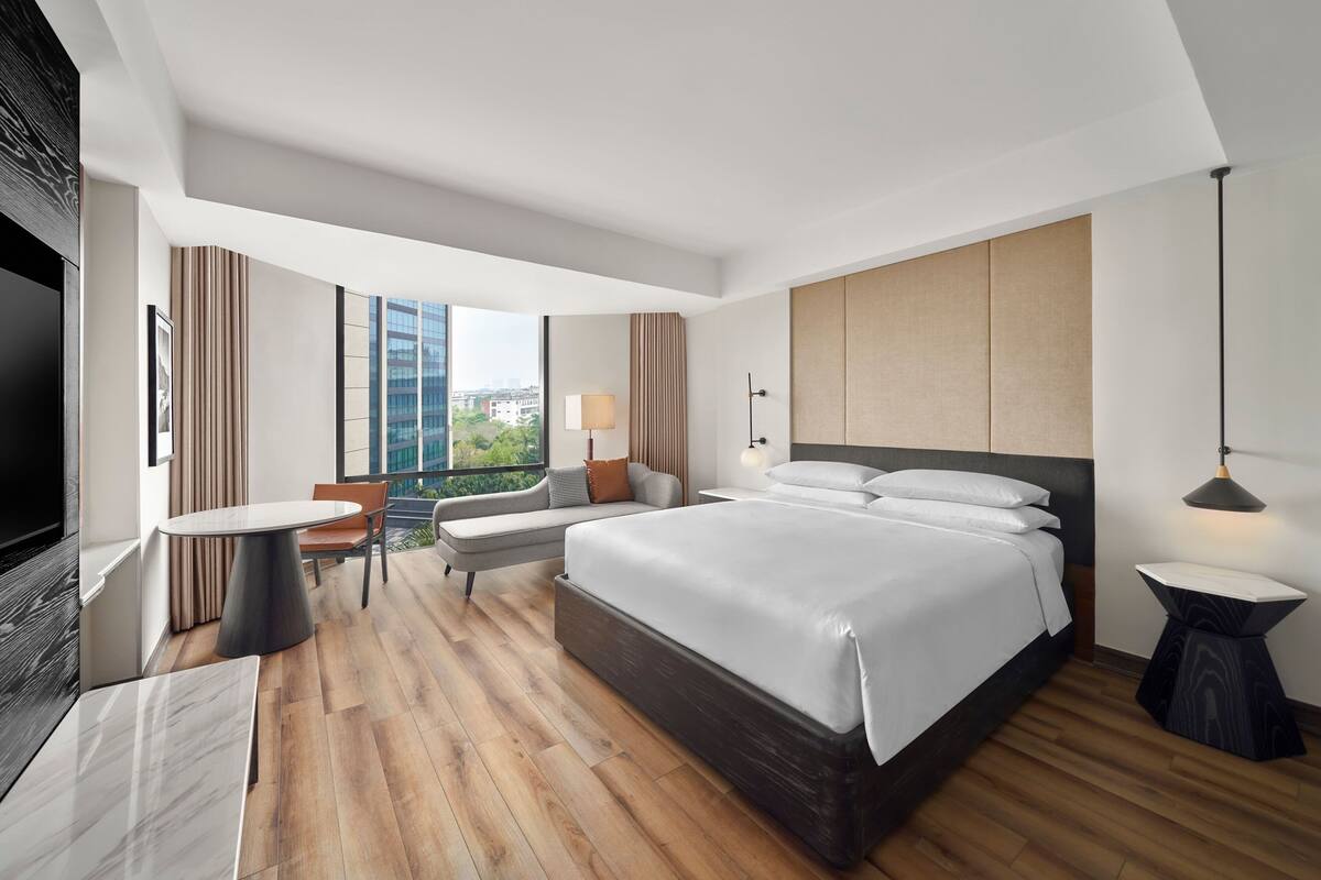 A modern hotel room with a large bed, a seating area with a table, and a TV.