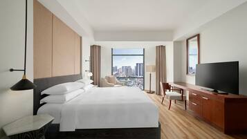 A hotel room with a large bed, a desk, a television, and a view of the cityscape.