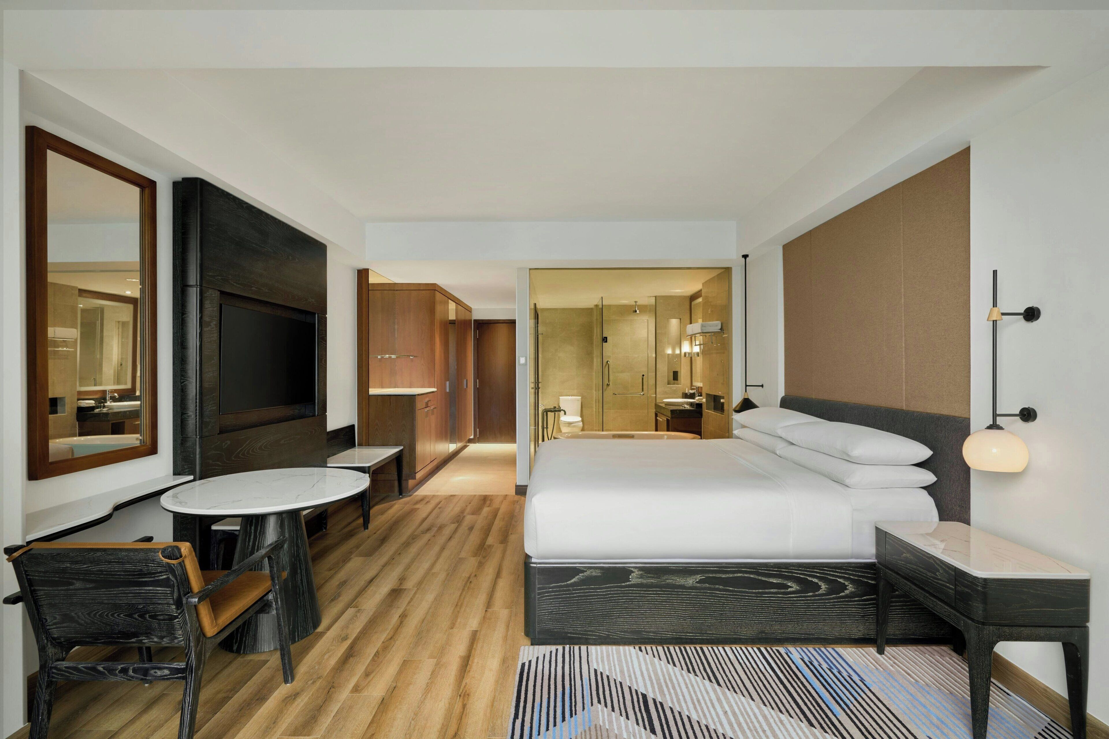 A modern hotel room with a large bed, a TV, a desk, and a chair.
