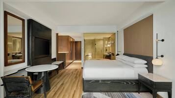 A modern hotel room with a large bed, a TV, a desk, and a chair.