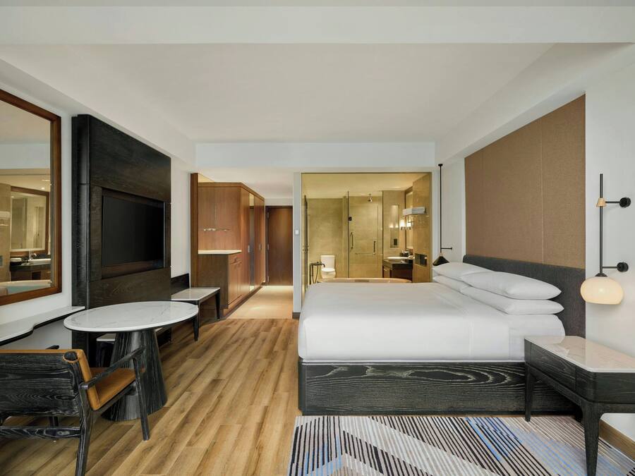 A modern hotel room with a large bed, a TV, a desk, and a chair.
