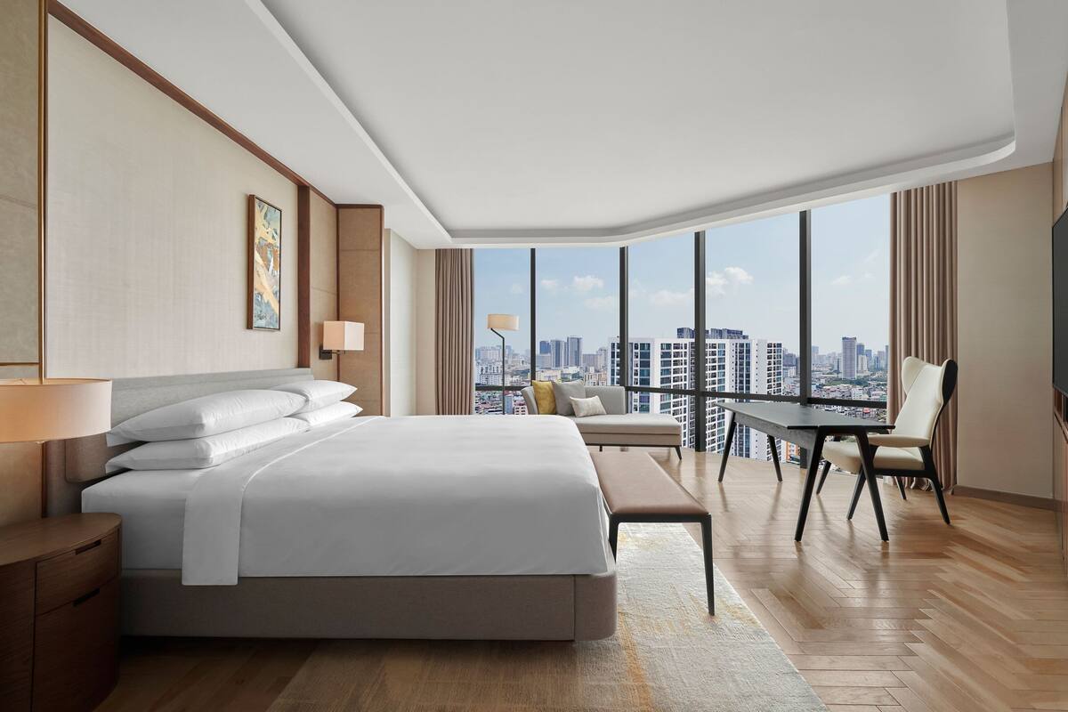 A modern hotel room with a large bed, a desk, and a view of the cityscape.