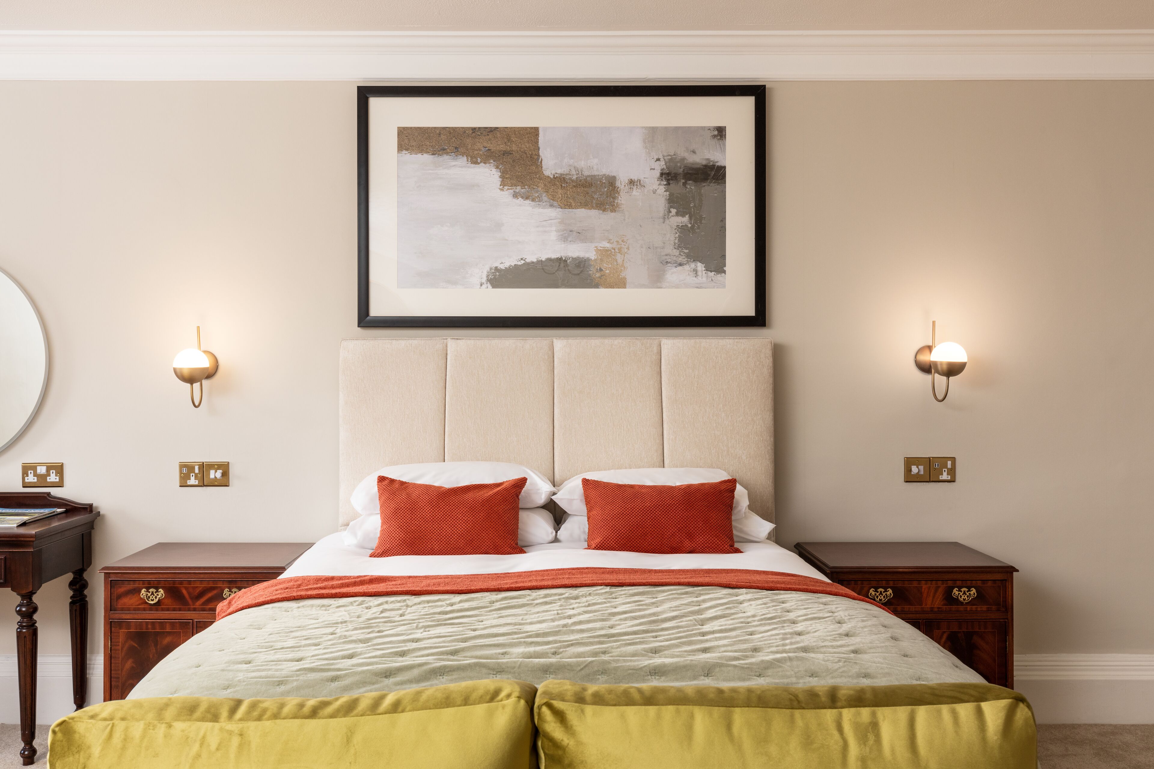 A neatly arranged bedroom with a large bed, two bedside tables, and a framed abstract painting above the bed.