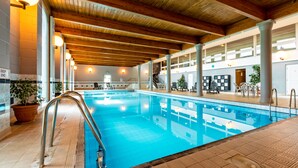 An indoor swimming pool with a wooden ceiling and tiled floor, surrounded by seating areas and potted plants. - Cally Palace Hotel & Golf Course (Castle Douglas)