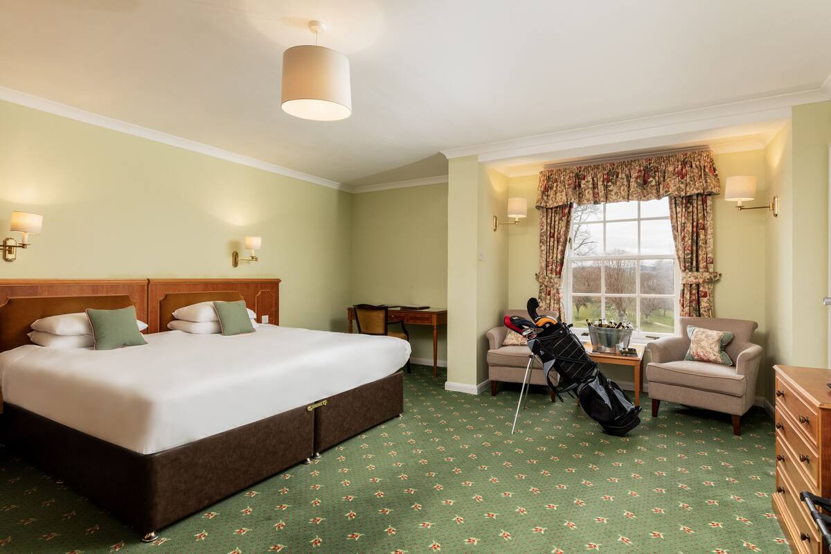 A hotel room with a large bed, a desk, a chair, and a view of the outdoors.