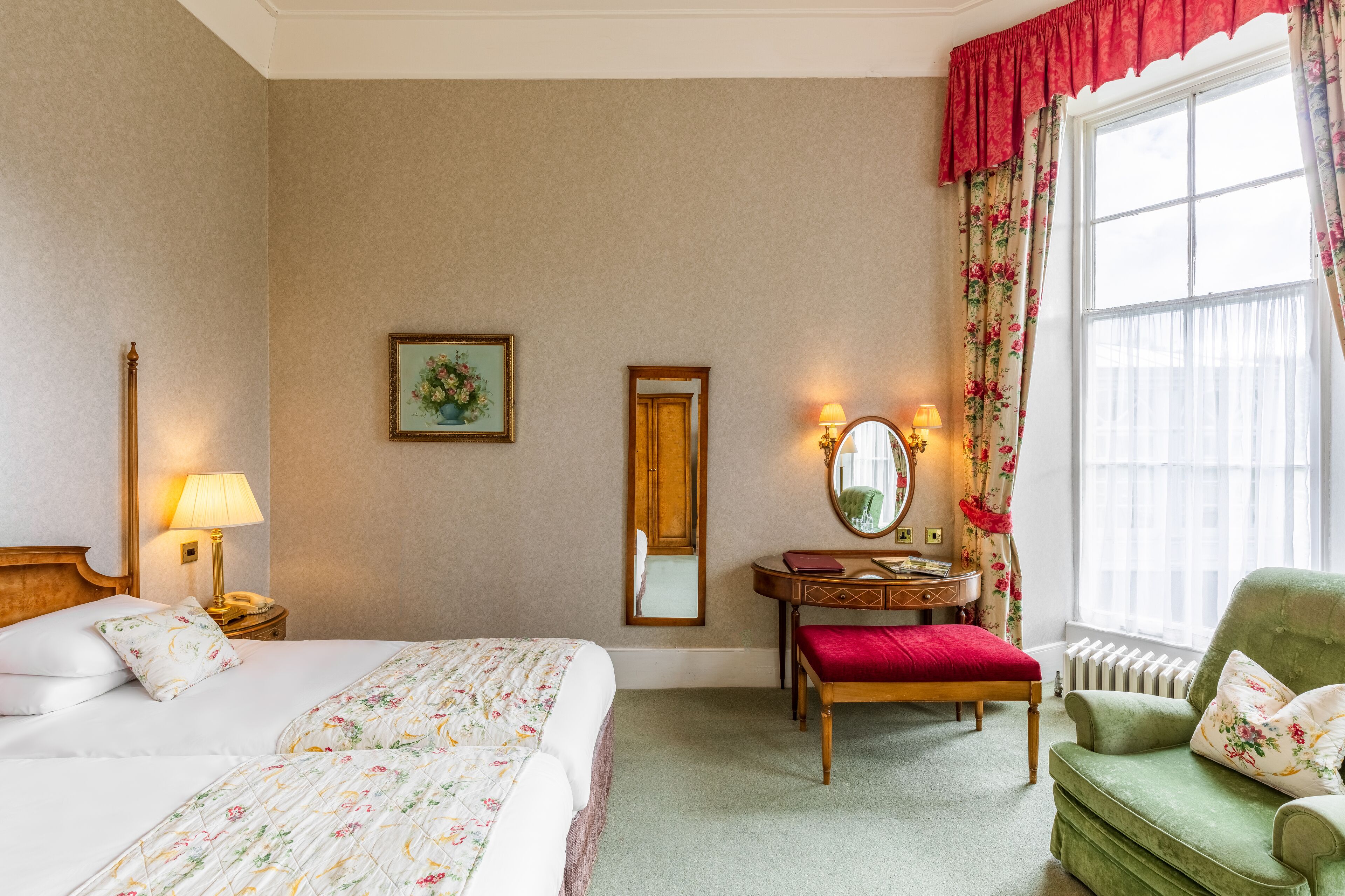 Habitación de hotel con cama, escritorio, silla, espejo y ventana con cortinas.