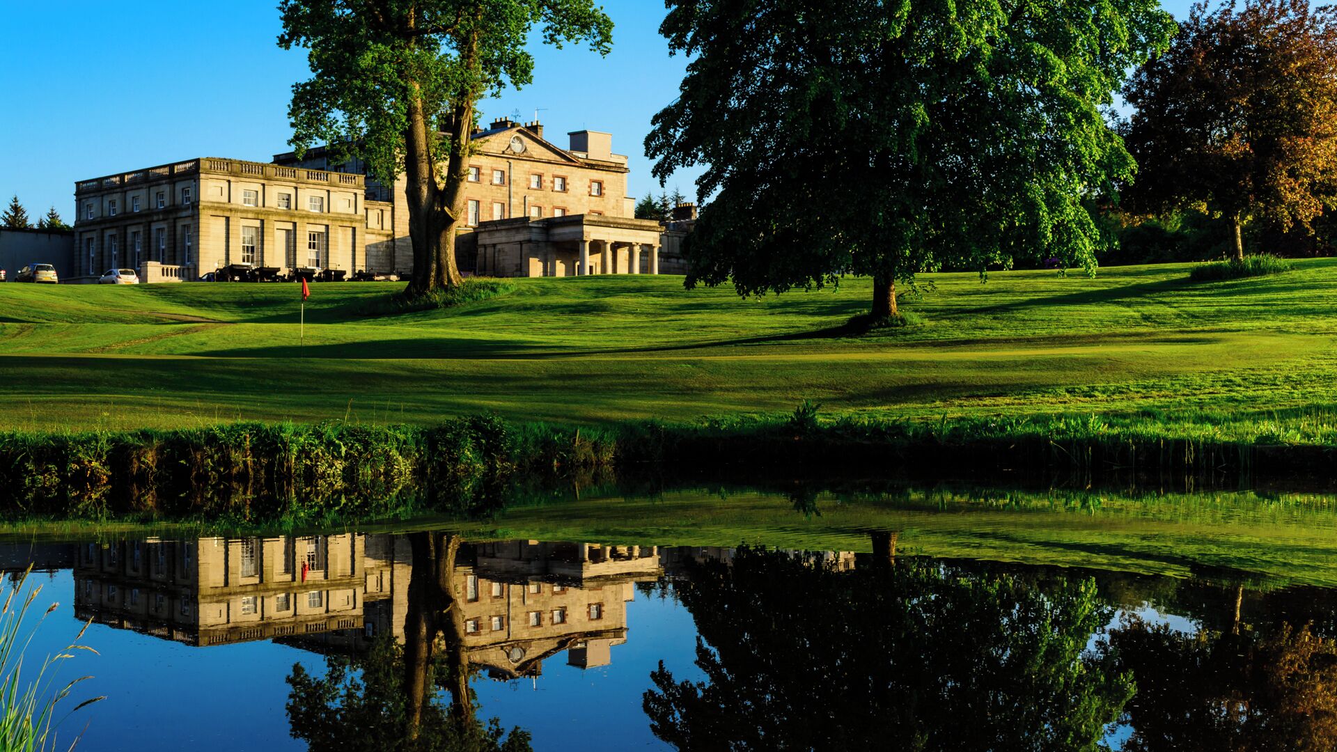 A large building with multiple windows and a reflection in a calm body of water.