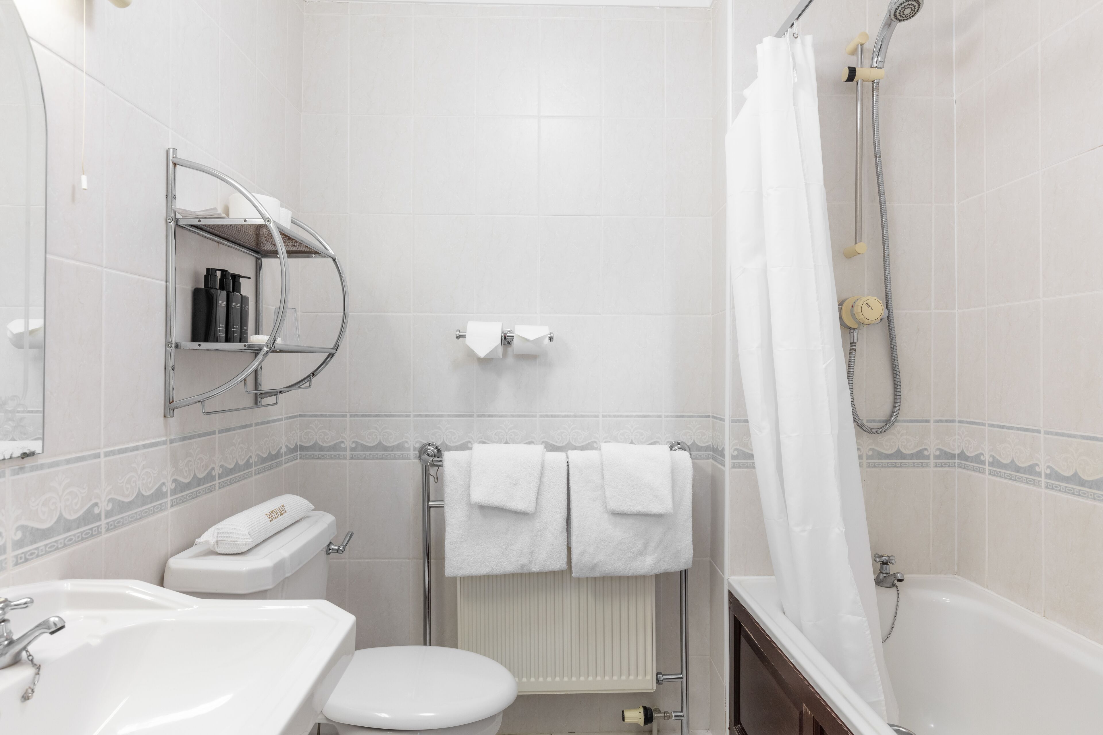 A bathroom with a toilet, sink, shower, and towel rack.