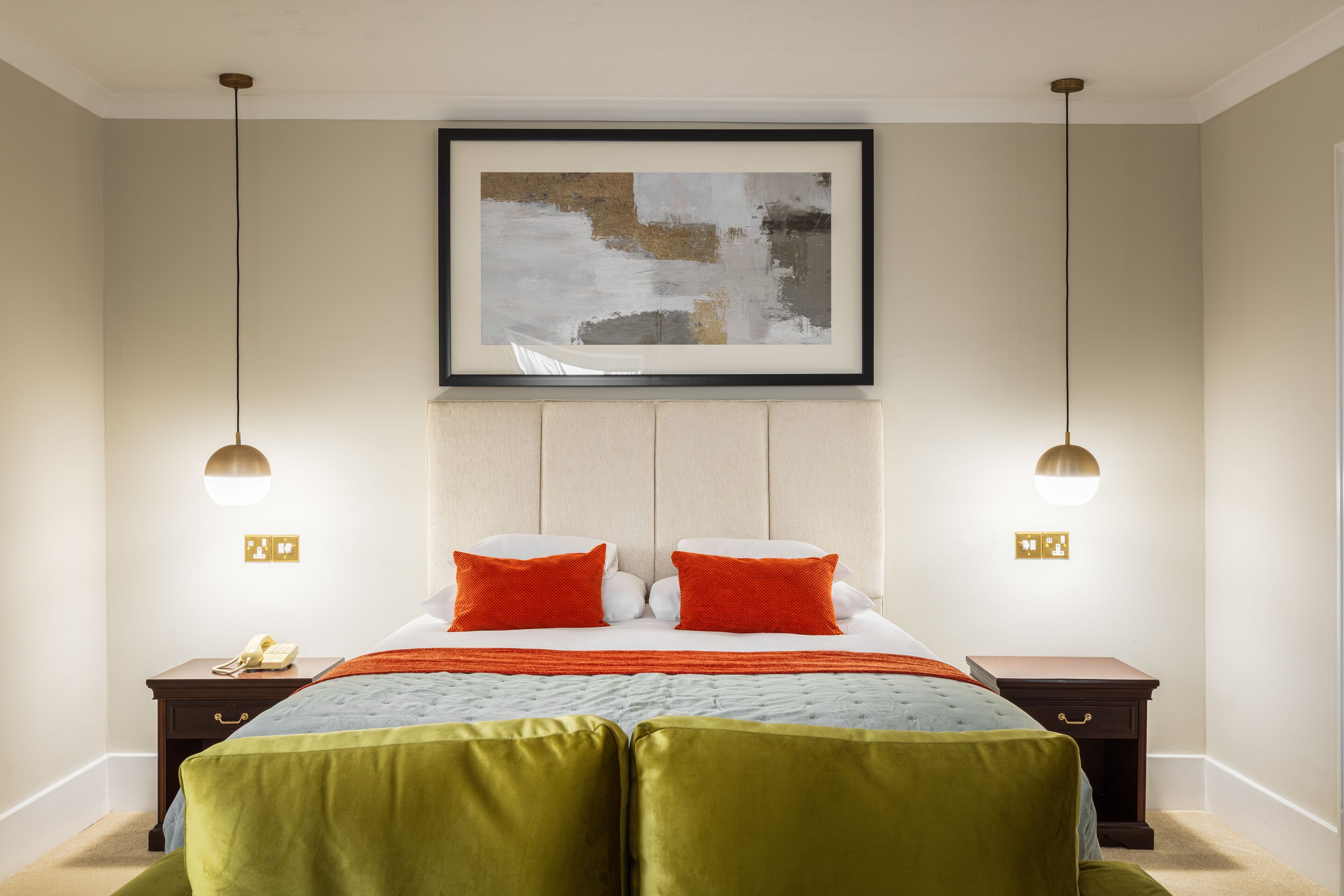 A hotel room with a large bed, two bedside tables, a framed abstract painting, and pendant lighting.