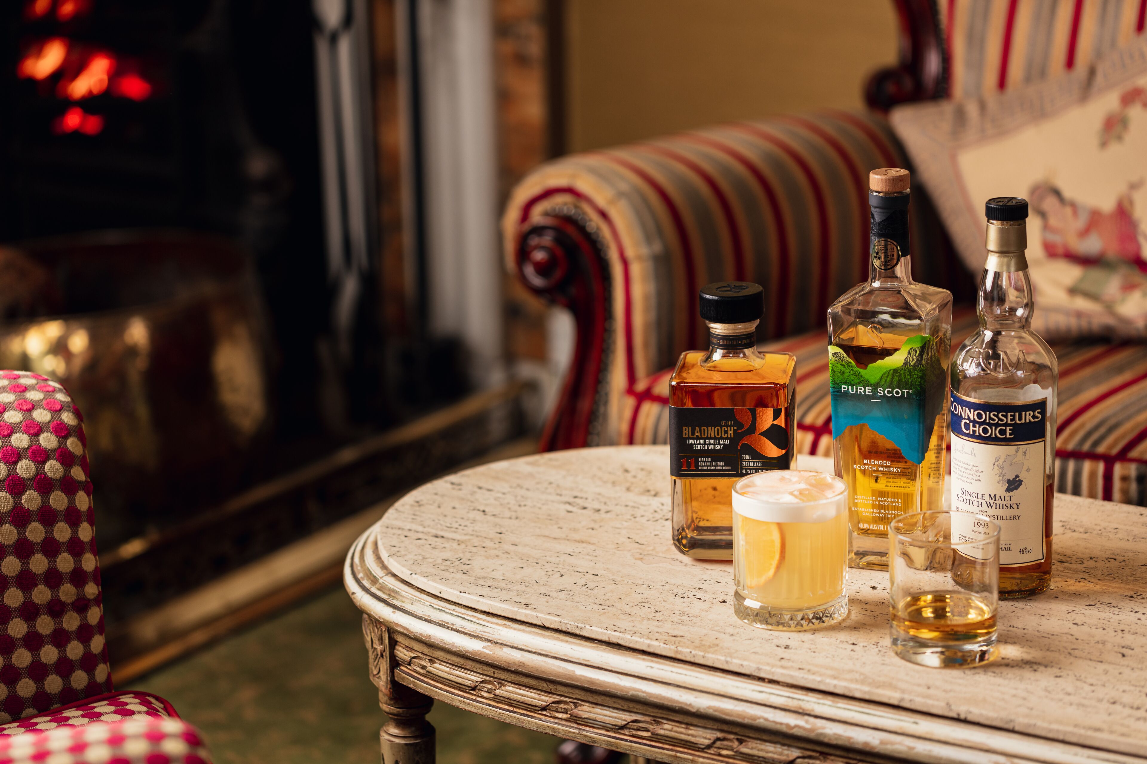 Une table ronde sur laquelle sont posées trois bouteilles de whisky et un verre de whisky.