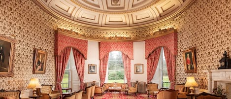 A grand room with ornate wallpaper, a red carpet, and classic furniture.