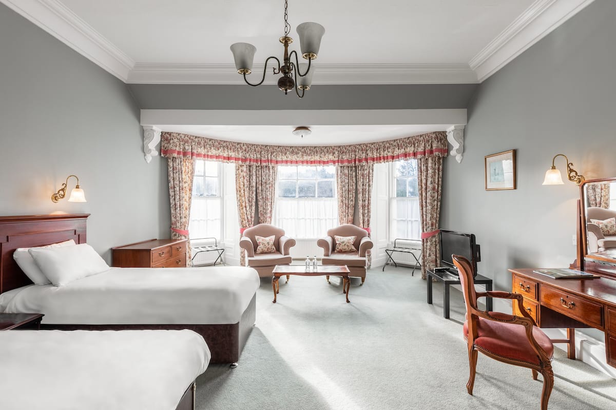A hotel room with two beds, a desk, a chair, a television, and a chandelier.