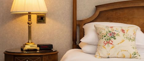 A neatly made bed with floral bedding, a wooden headboard, and a bedside table with a lamp and a clock.