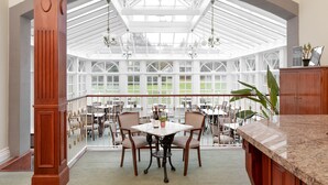 A spacious conservatory with a high ceiling, large windows, and a central dining table surrounded by chairs. - Cally Palace Hotel & Golf Course (Castle Douglas)