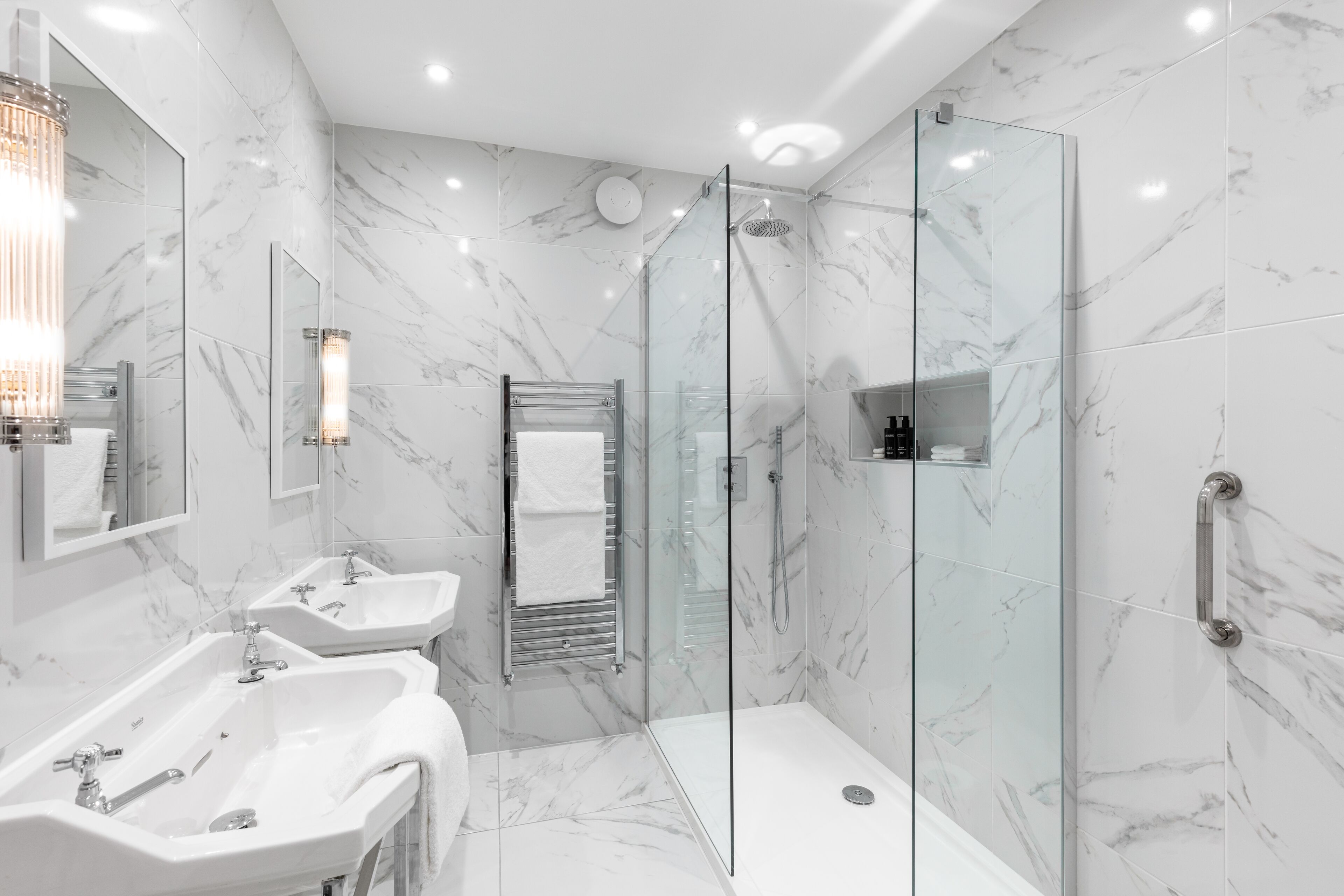 Un baño moderno con paredes de mármol, dos lavamanos, un box de ducha de cristal y una ducha a pie.