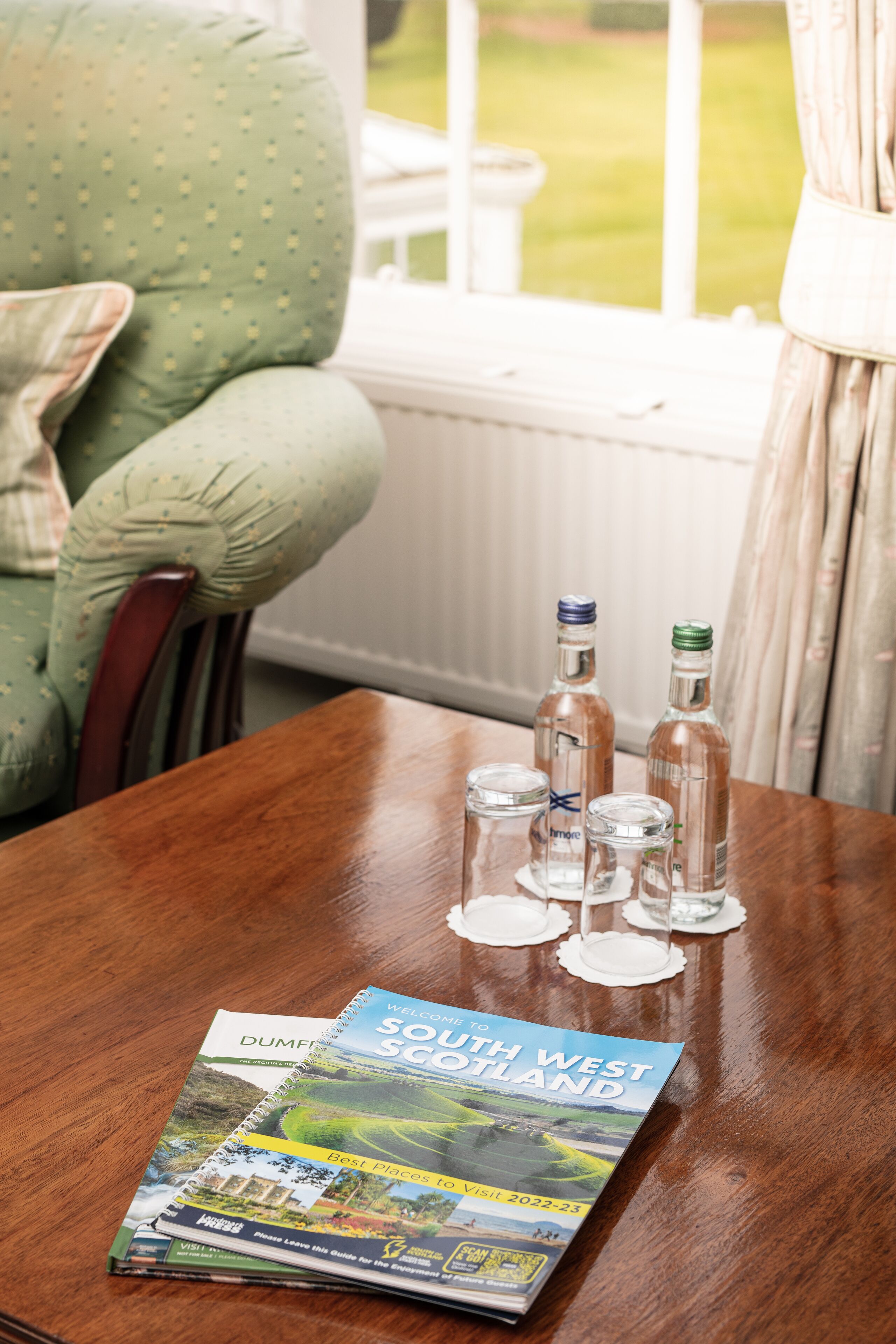 A wooden table with a brochure titled "Welcome to South West Scotland" and three bottles of alcohol.
