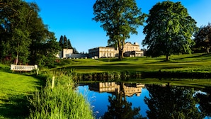 A large building with a reflection in a pond, surrounded by lush greenery and trees. - Cally Palace Hotel & Golf Course (Castle Douglas)