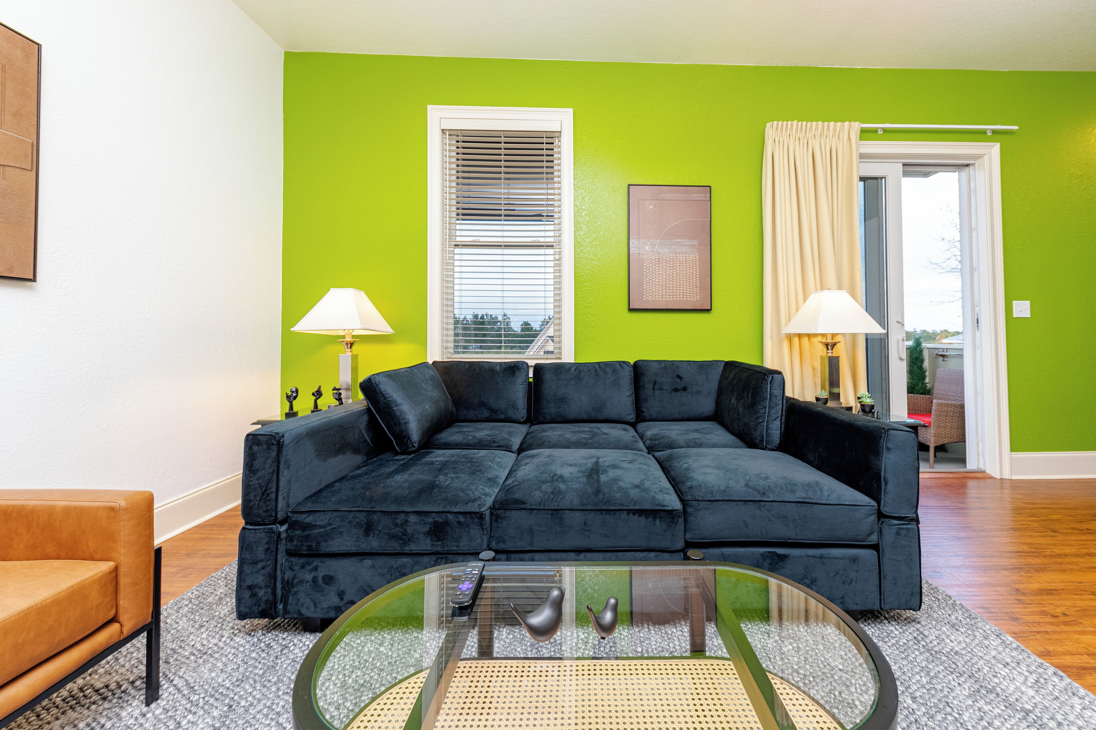 A living room with a black velvet sofa, a glass coffee table, and a green wall.