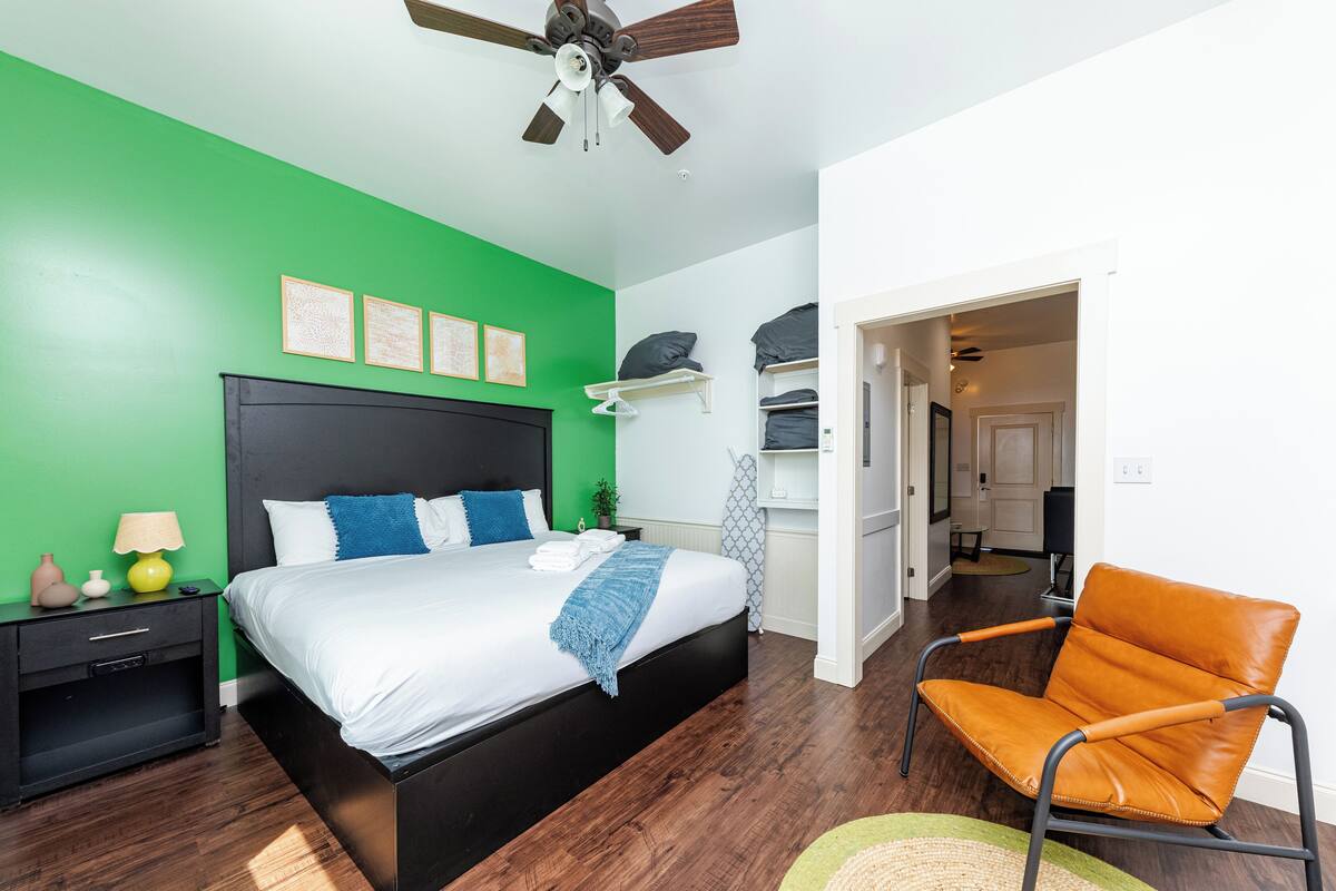 A bedroom with a bed, a nightstand, a chair, a ceiling fan, and a green wall.