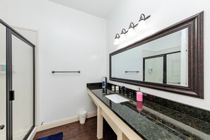 A bathroom with a large mirror, a sink, and a shower area. - 30A Inn & Suites (Santa Rosa Beach)