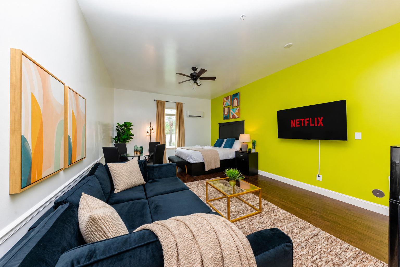 A modern living room with a dark blue sofa, a coffee table, and a TV mounted on a bright green wall.