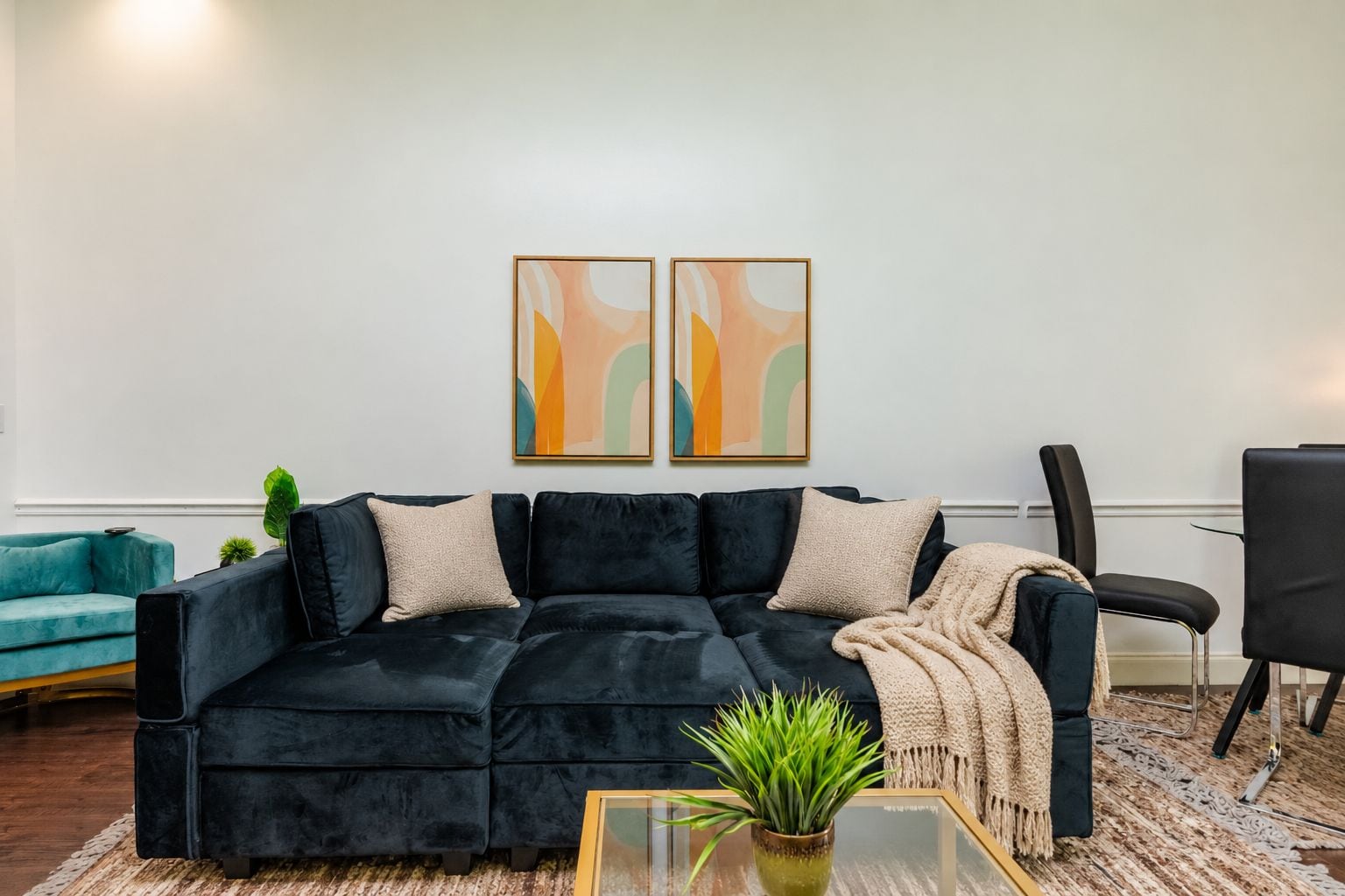 A living room with a dark velvet sectional sofa, a glass coffee table, and two abstract paintings on the wall.