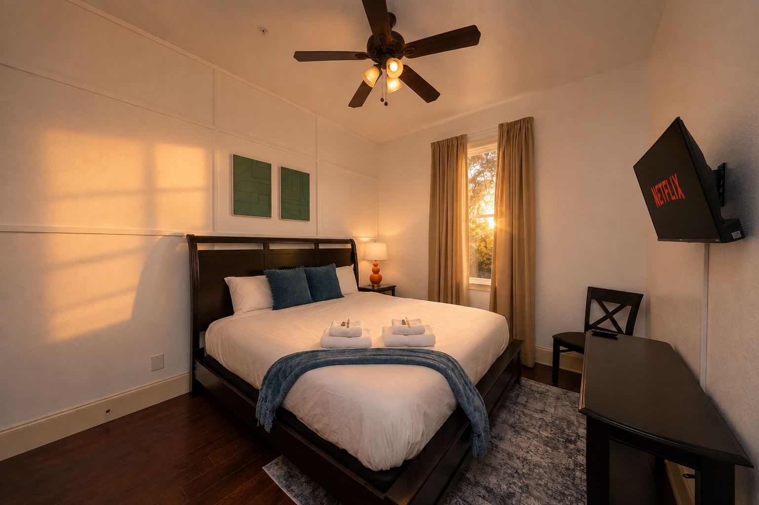 A hotel room with a bed, a desk, a ceiling fan, and a television.